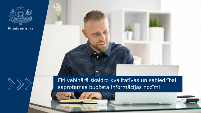 Vīrietis zilā kreklā sēž pie galda, veic pierakstus uz galda esošā pierakstu blokā, uz galda stāv portatīvais dators. 
