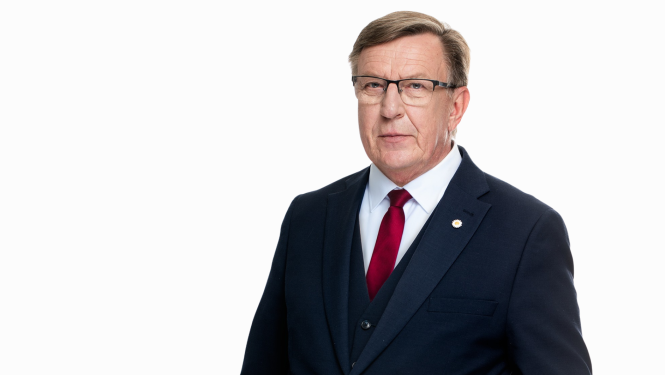 Portreta foto ar Māri Kučinski. Viņš ir ģērbies tumši zilā uzvalkā ar baltu kreklu un sarkanu kaklasaiti, ir brilles.