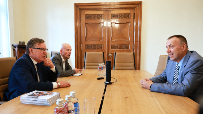Darba tikšanās sanāksmju telpā, kurā trīs vīrieši uzvalkos apspriež jautājumus pie konferenču galda