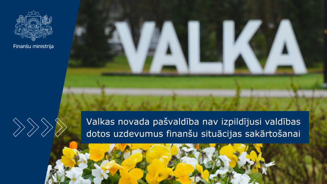 Dabā stāvošs VALKAS pilsētas uzraksts - burti, priekšplānā ir redzami ziedi. Uz attēla ir teksts