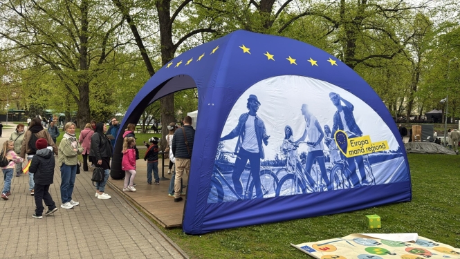 Apdrukāta telts parkā, cilvēki iet iekšā un nāk ārā no telts
