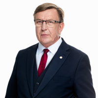 Portreta foto ar Māri Kučinski. Viņš ir ģērbies tumši zilā uzvalkā ar baltu kreklu un sarkanu kaklasaiti, ir brilles.