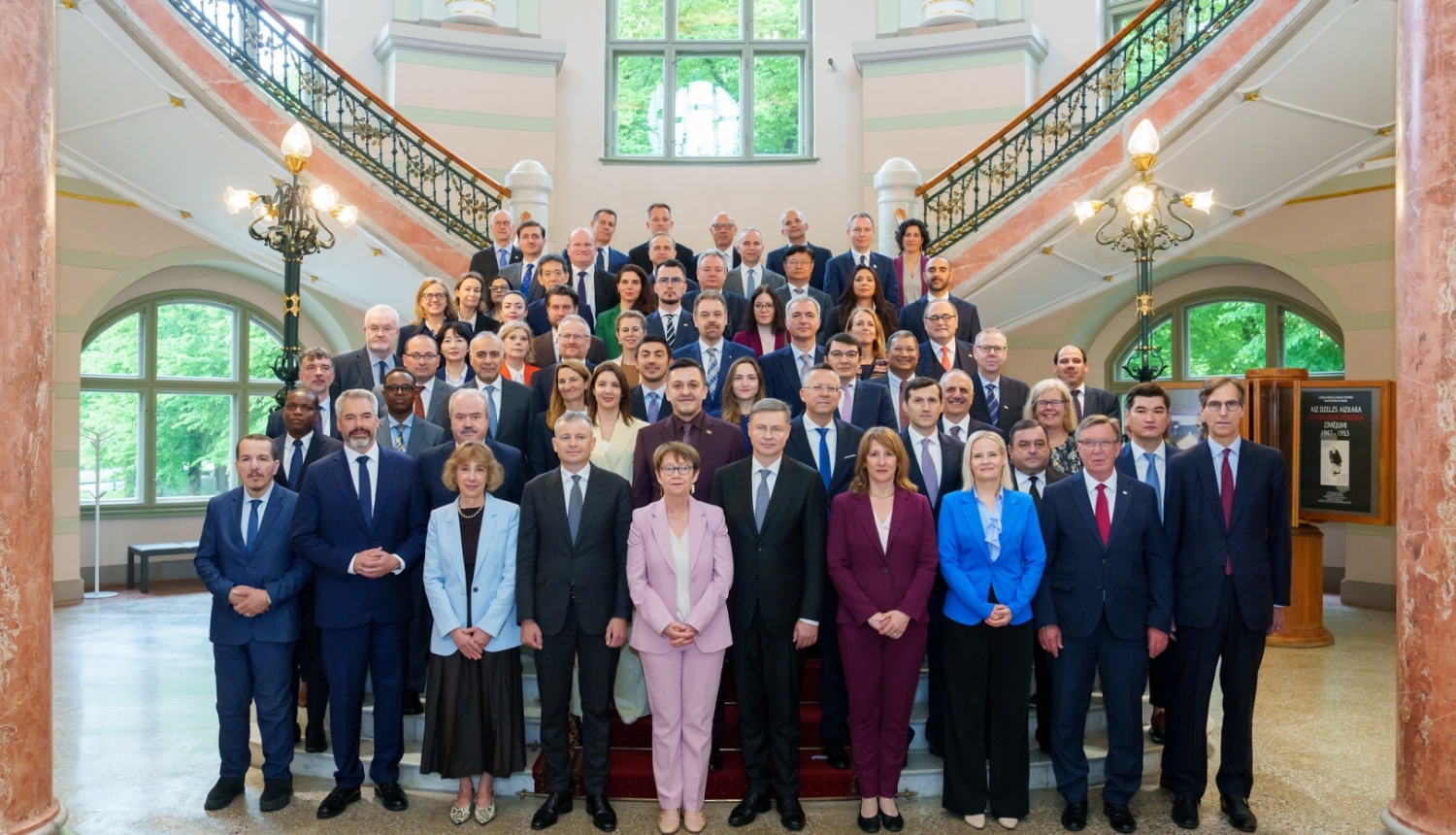 Uz Mākslas muzeja kāpnēm vairākās rindās stāv vīrieši un sievietes lietišķā apģērbā