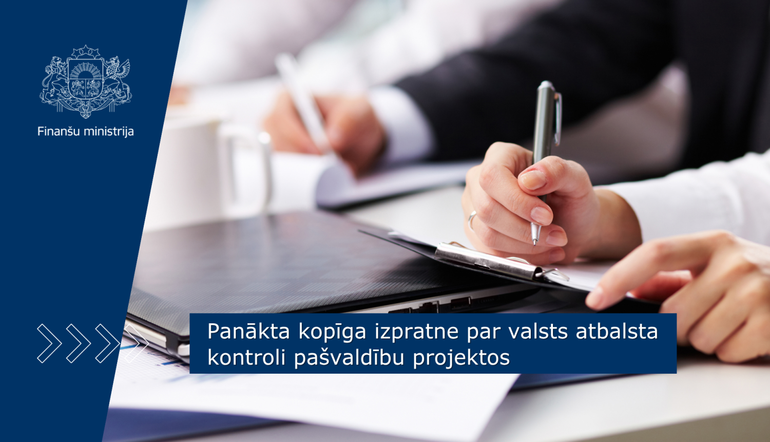 Divi cilvēki darba sanāksmē raksta piezīmes uz dokumentiem pie galda ar klēpjdatoru
