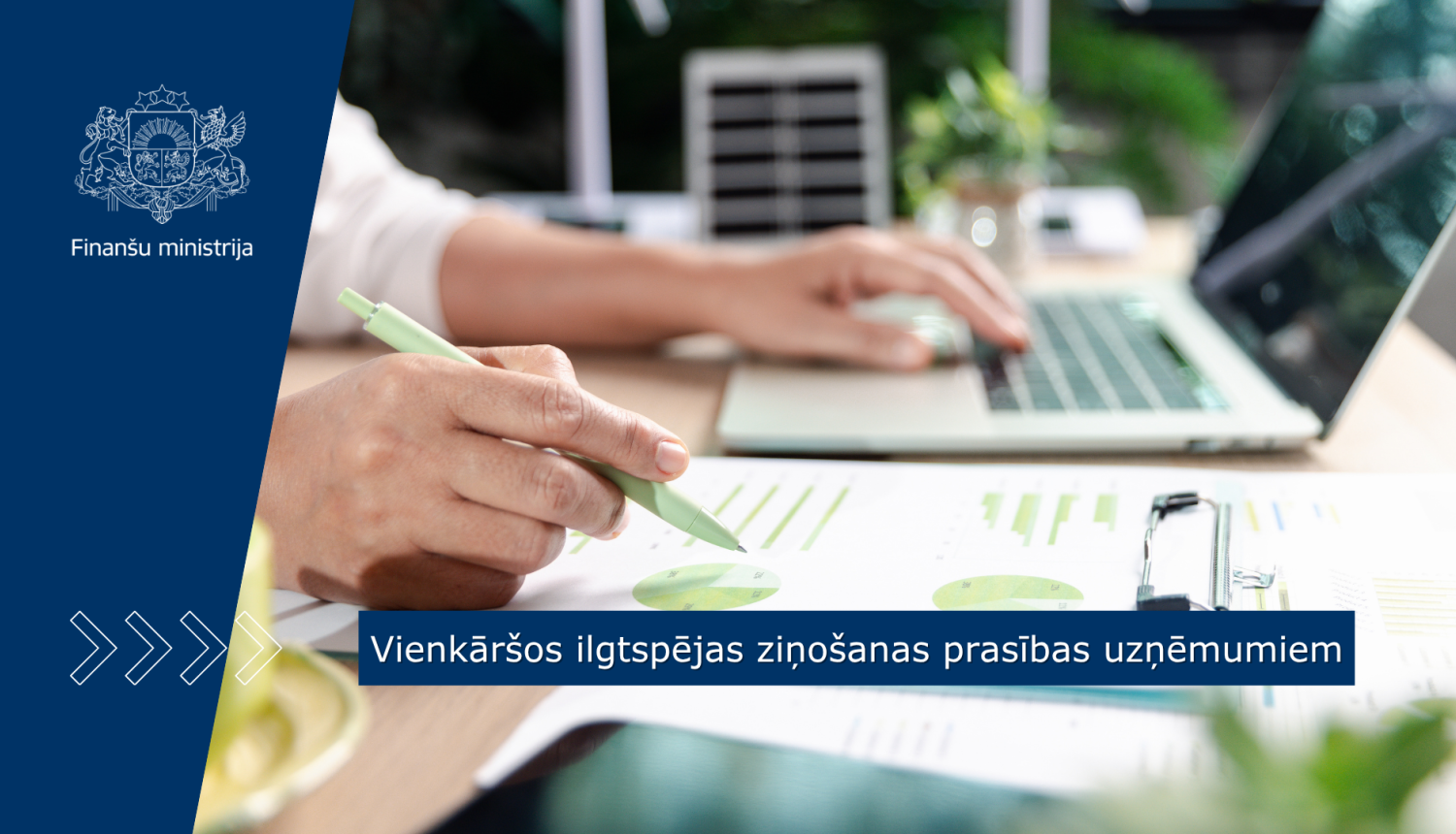 Uz darba galda virsmas ir portatīvais dators un dokumenti, cilvēks ar pildspalvu veic pierakstus