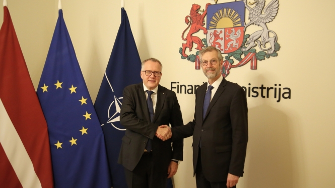 Divi vīrieši sarokojas uz Latvijas, ES un NATO karogu un ģērboņa fona