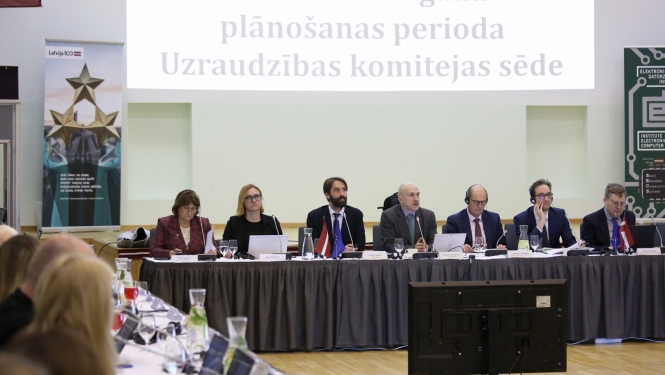 Vīrieši un sievietes lielā zālē sēž pie gara galda