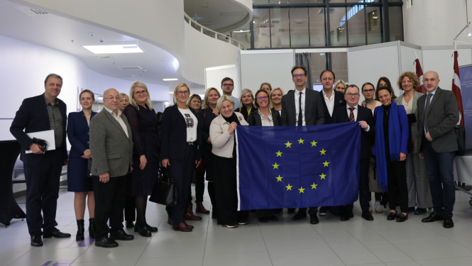 Attēlā redzama cilvēku grupa, priekšplānā esošie cilvēki rokās tur izklātu ES karogu 