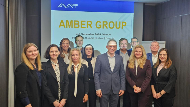 Attēlā redzama grupa cilvēku, kuri stāv vairākās rindās, viņiem aiz muguras redzams projektora eksrāns