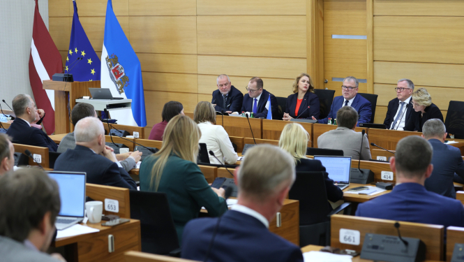 Pie gara galda auditorijas priekšā sēž seši cilvēki, kuri diskutē ar auditoriju, telpas malā stāv Latvijas ES un Rīga domes karogi