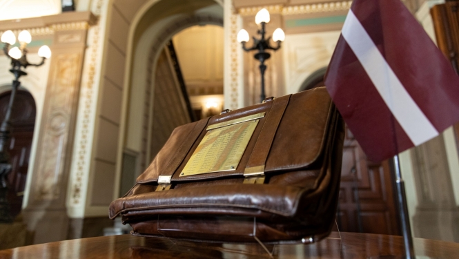 Valsts budžeta portfelis stāv uz galda blakus Latvijas karogam uz statīva.
