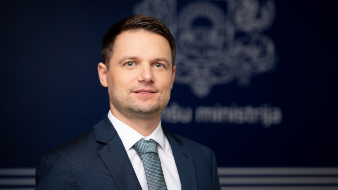 Vīrieša zilā uzvalkā ar kaklasaiti portrets uz zila fona ar Finanšu ministrijas ģērboni