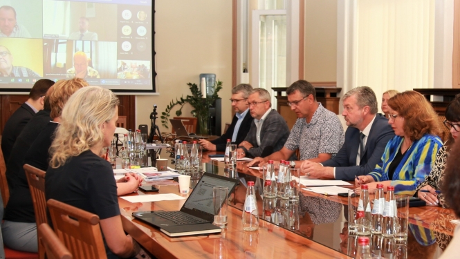Sanāksme. Pie darba galda redzami vīrieši un sievietes diskutējam