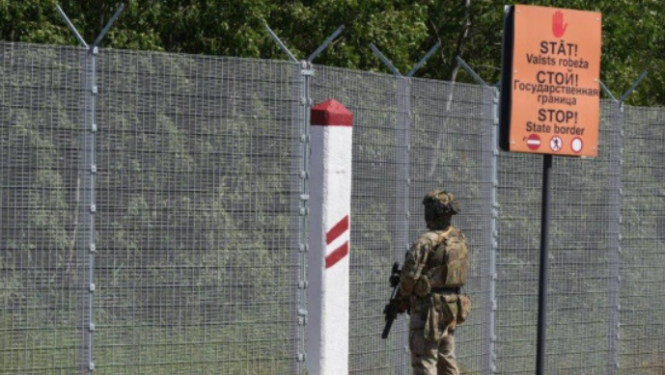 Valsts robeža ar brīdinošiem uzrakstiem un zemessargu no mugurpuses