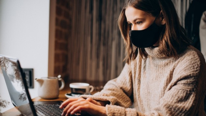 Sieviete sejas maskā strādā pie datora