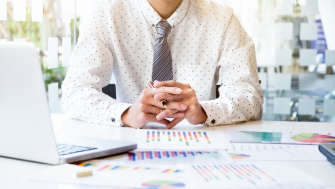 vīrietis pie datora ar dokumentiem