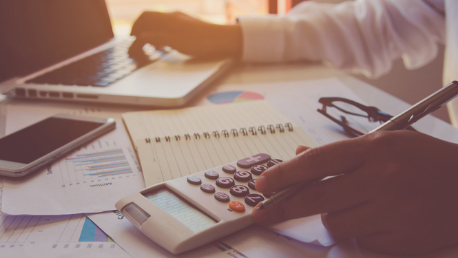 Darba galds, kurā vīrietis veic aprēķinus uz kalkulatora 