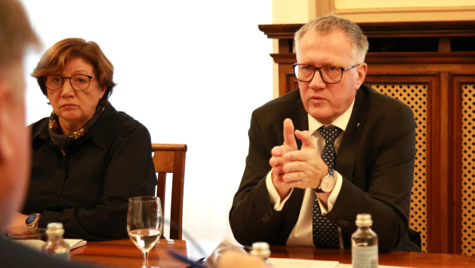 Finanšu ministrs A.Ašeradens un Inta Komisare sēž pie galda un sarunājas ar cilvēku otrpus galdam