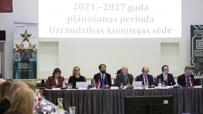 Vīrieši un sievietes lielā zālē sēž pie gara galda