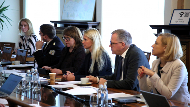 Pie galda rindā  sēž sievietes un vīrieši un sarunājas