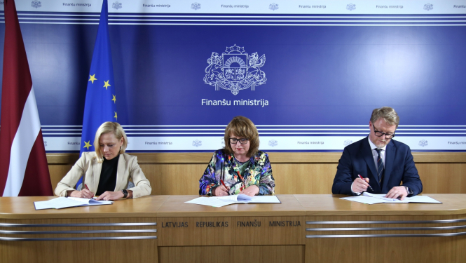 Divas sievietes un vīrietis sēž pie galda un paraksta dokumentus