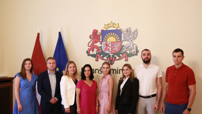 Cilvēki rindā stāv pie karogiem 