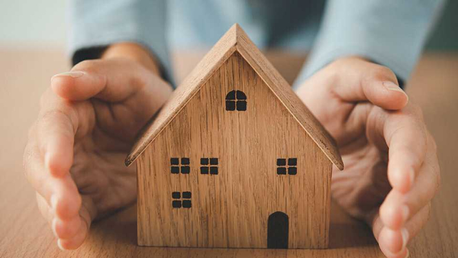 Attēlā redzama neliela koka māja, kas aptverta rokām