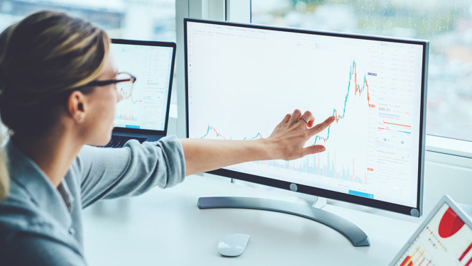 Sieviete ar brillēm rāda ar pirkstu uz grafikiem datorā