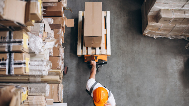 Darbinieks noliktavā pārvieto kastes