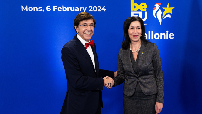 vīrietis melnā uzvalkā ar sarkanu tauriņu sarokojas ar sievieti tumšā kostīmā uz zila fona