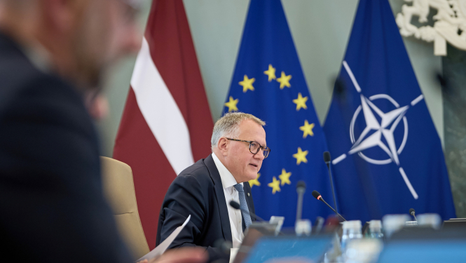 Attēla centrā finanšu ministrs Arvils Ašeradens Ministru kabineta sēžu zālē, fonā Latvijas, Eiropas Savienības un NATO karogi