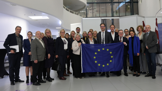 Attēlā redzama cilvēku grupa, priekšplānā esošie cilvēki rokās tur izklātu ES karogu 