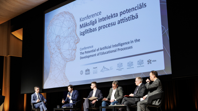 Attēlā redzami seši vīrieši, kuri sēž krēslos uz skatuves un savstarpēji diskutē, fonā milzīgs projektora ekrāns