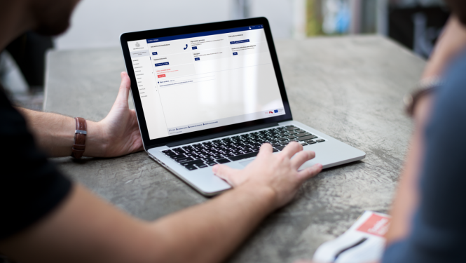 Tuvplānā redzams portatīvais dators, kurš novietots uz galda, ekrānā redzama VID tīmekļvietne