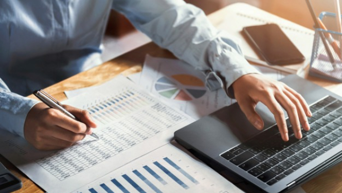 vīrietis ar datoru un dokumentiem veic aprēķinus