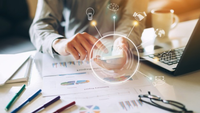 cilvēks pie darba galda ar datoru, telefonu un grafikiem