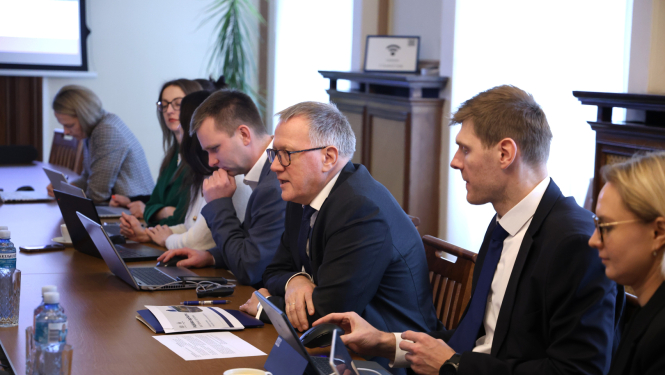 Pie galda sēž vīrieši un sievietes, kas savstarpēji diskutē