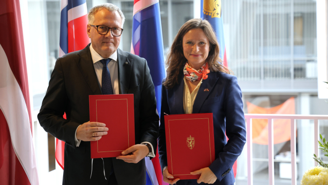 Vīrietis un sieviete uz karogu fona stāv līdzās un smaida, rokās turot dokumentu mapes