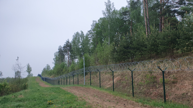 Attēlā redzams dabasskats ar žogu un dzeloņstiepļu joslu