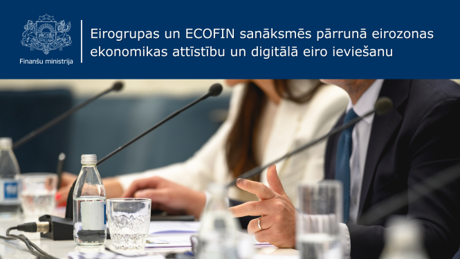 Attēlā redzami vīrietis un sieviete, kuri sēž pie galda, vīrietis žestikulē, uz galda stāv mikrofoni, dokumenti un ūdens pudeles ar glāzēm