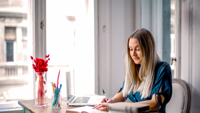 Sieviete pie galda ar datoru un grāmatām