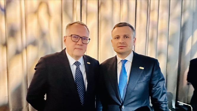 Divi vīrieši tumšos uzvalkos stāv blakus