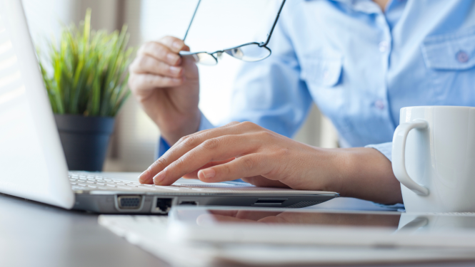 Tuvplānā sievietes rokas, kuras strādā ar portatīvo datoru, līdzās redzama tējas krūze un telpaugs