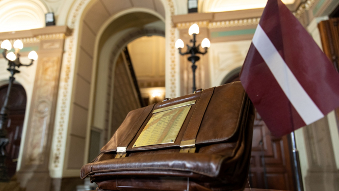 Valsts budžeta portfelis stāv uz galda blakus Latvijas karogam uz statīva.