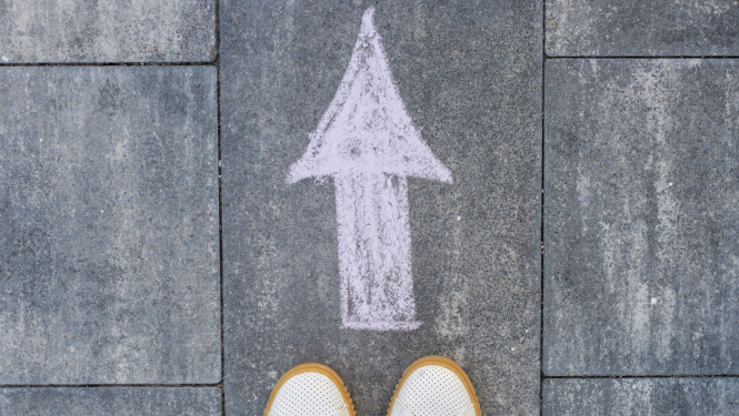 Uz asfalta uzzīmēta bulta un cilvēka pēdas pie tās 