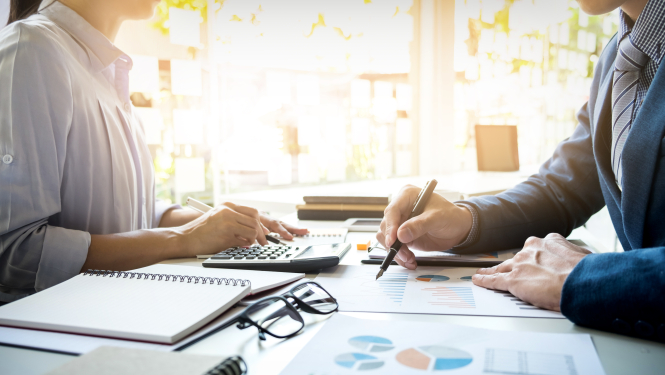 Vīrietis un sieviete sēž pie darba galda un veic aprēķinus