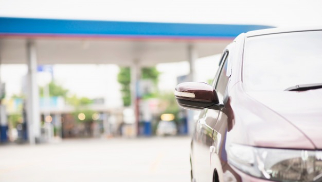 Automašīna ar degvielas uzpildes staciju fonā