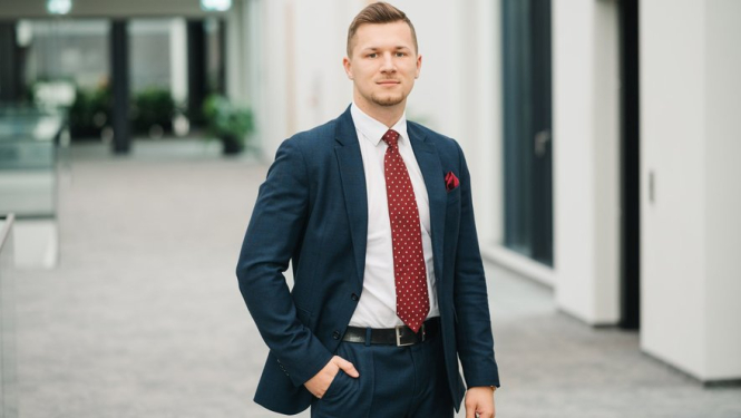 Jauns vīrietis tumšā uzvalkā, baltu kreklu un sarkanu kaklasaiti