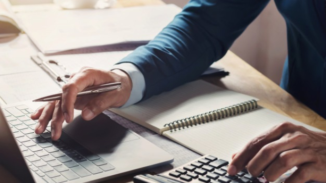 Vīrieša rokas pie galda ar datoru, kalkulatoru