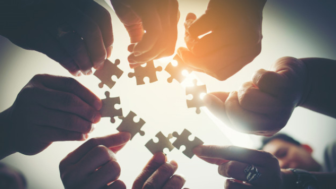 vairāki cilvēki stāv aplī un tur rokās izstieptu puzles gabalu